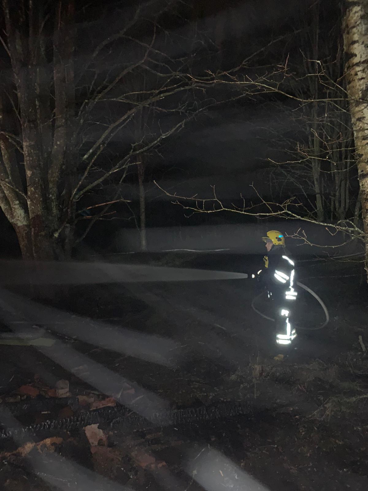 Palokuntalainen suihkuttaa letkulla vettä pimeässä heijastimet hohtaen.