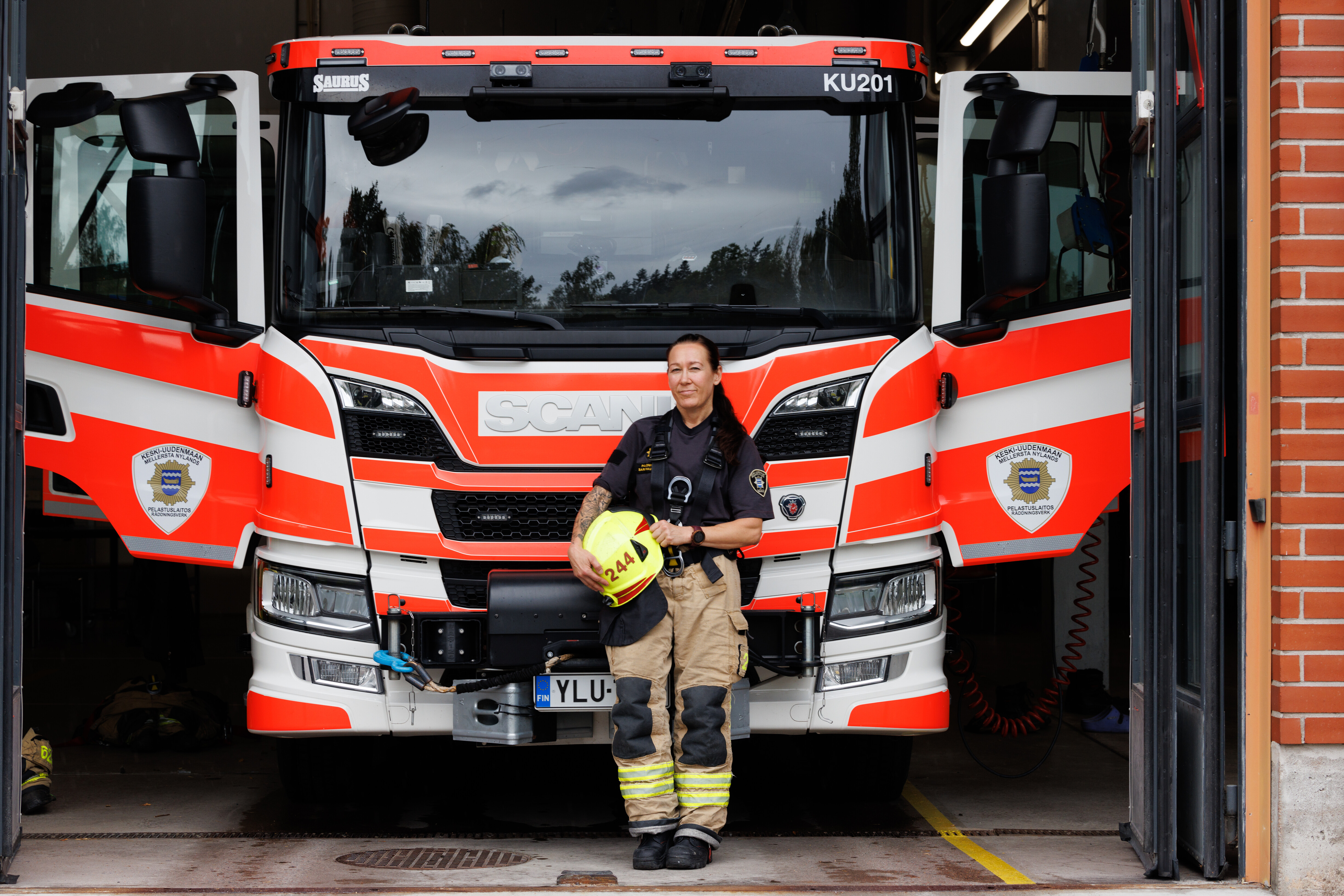 Sari Rautiala pelastajan varusteissa, kypärä kädessä paloauton edessä.
