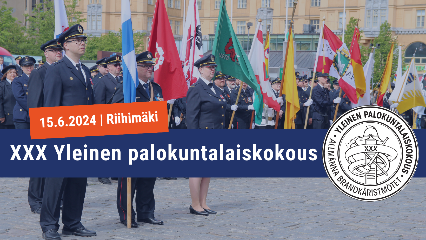 Palokuntalaiset seisovat rivissä paraatissa ja pitävät pystyssä palokuntien lippuja.