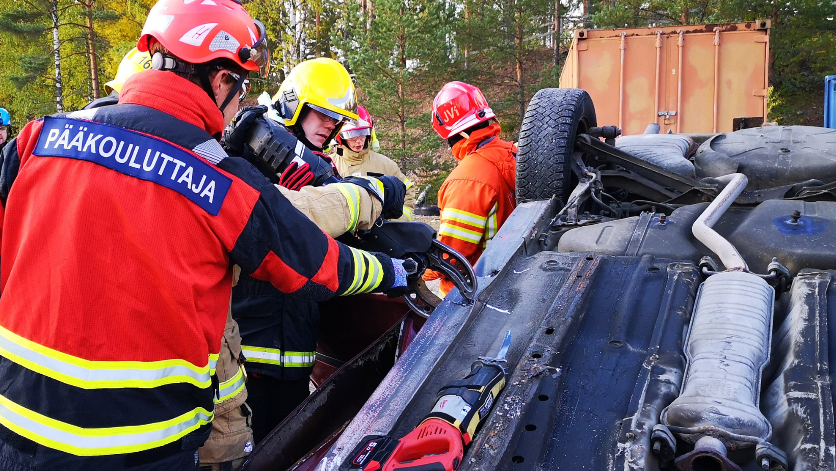 Palokuntalainen pääkouluttaja-teksti selässään neuvoo toista palokuntalaista ajoneuvosta pelastamisen koulutuksessa.