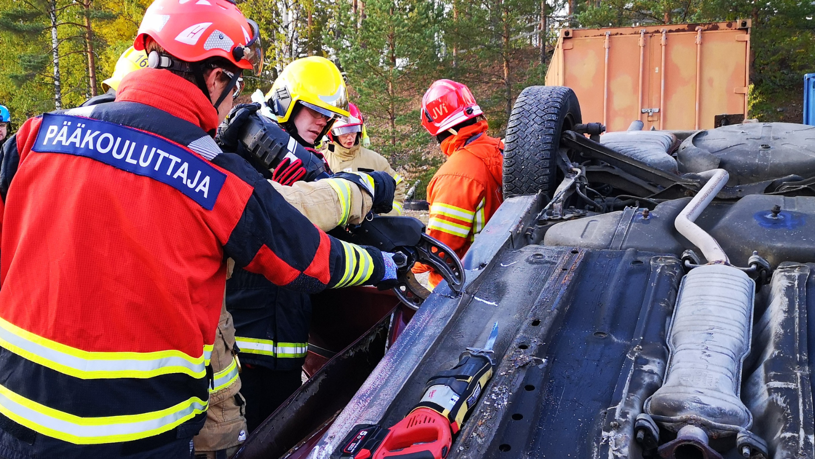 Kuvassa palokuntalainen jonka takin selässä lukee pääkouluttaja, antaa ohjeita toiselle palokuntalaiselle ajoneuvosta pelastamistekniikan kurssilla.