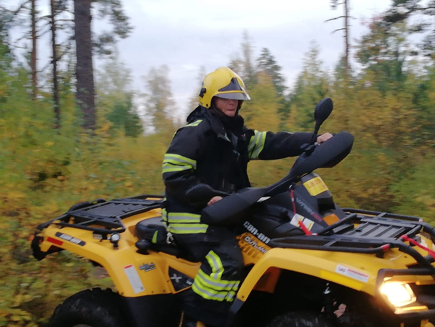 Nainen ajaa palokuntavarusteisiin pukeutuneena mönkijällä metsässä.