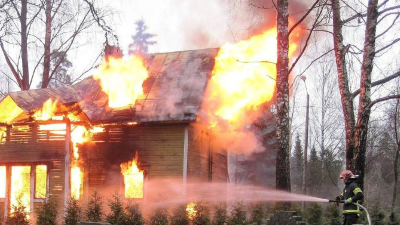 Palokuntalainen suihkuttaa letkulla vettä palavaan taloon.
