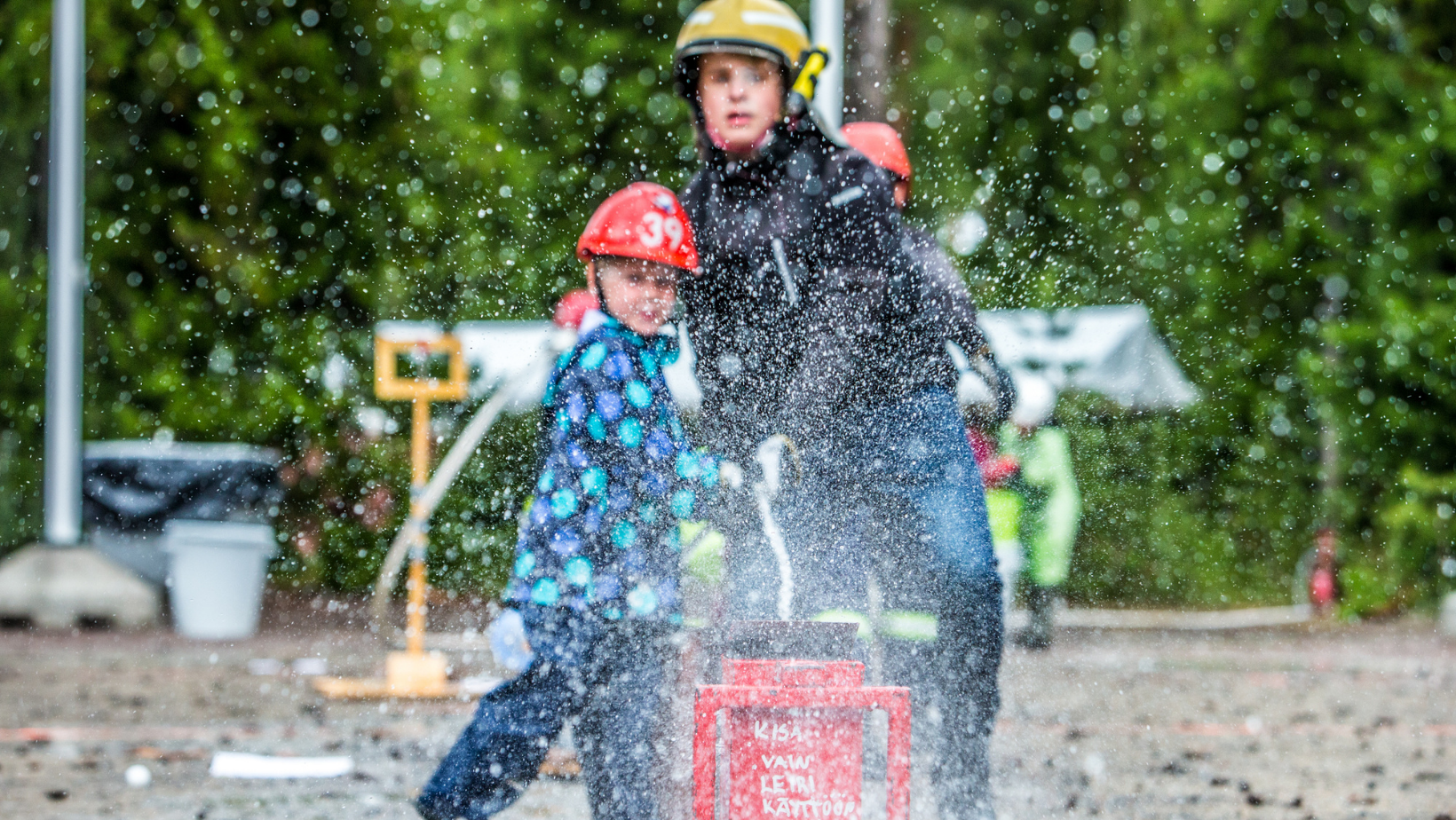 Kuvassa kaksi palokuntanuorta, jotka käyttävät sankoruiskua.