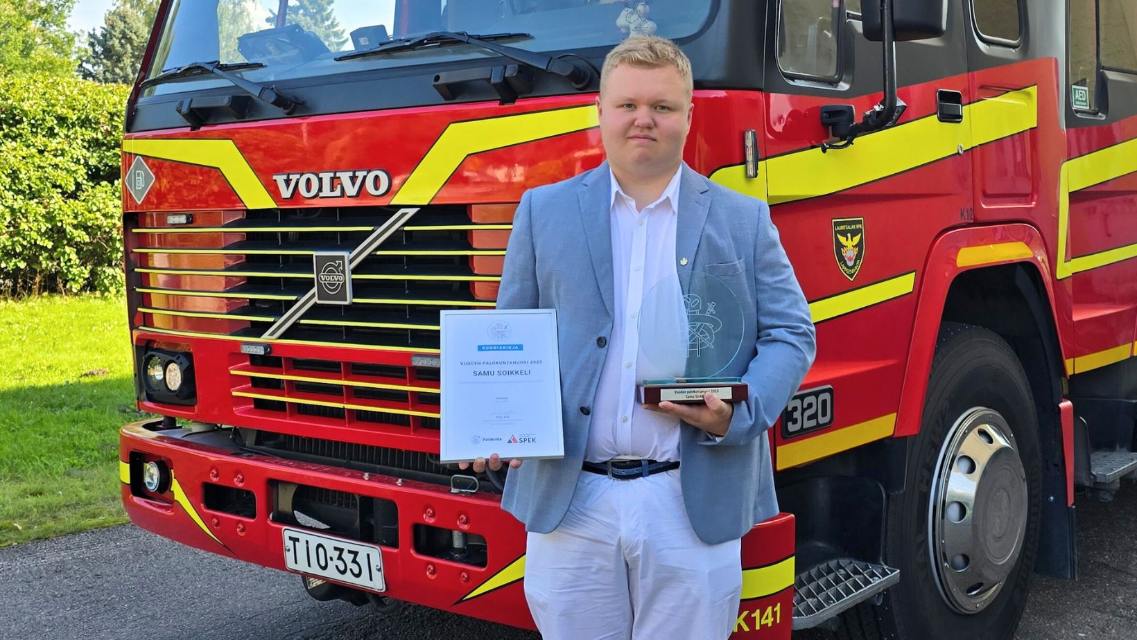 Kuvassa Vuoden palokuntanuori 2023 valittu Samu Soikkeli poseeraa paloauton edessä kunniakirjan ja palkinnon