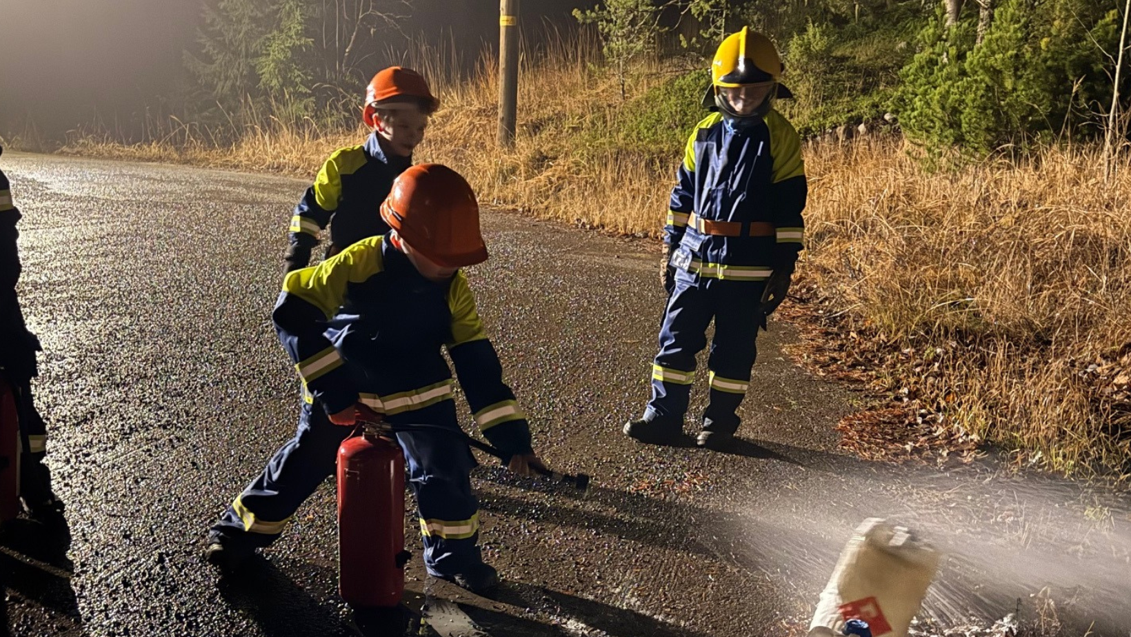 Kolme palokuntanuorta syyssäässä ulkona harjoittelemassa käsisammuttimen käyttöä
