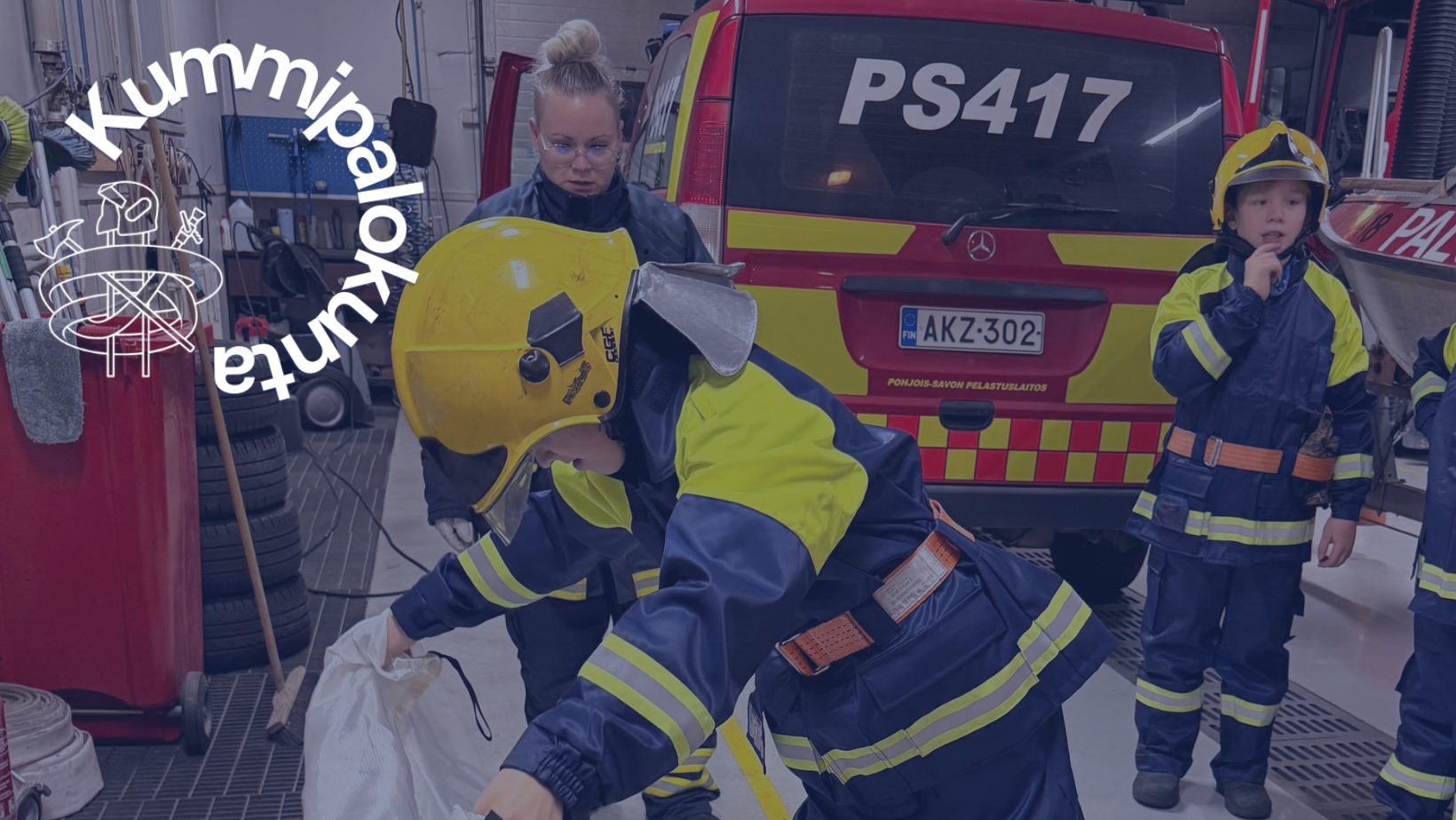 Palokuntanuori harjoittelee sammutuspeitteen käyttöä. Takana kouluttaja ja toinen palokuntanuori sekä palokunnan miehistönkuljetusauto.