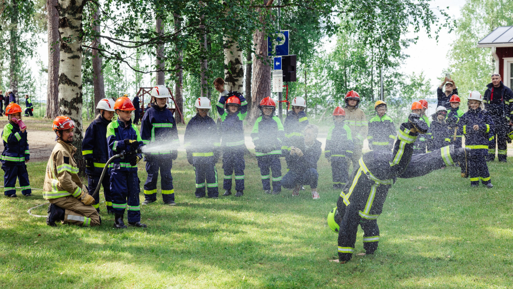 Palokuntanuoret kastelevat kouluttajan vesisuihkulla.
